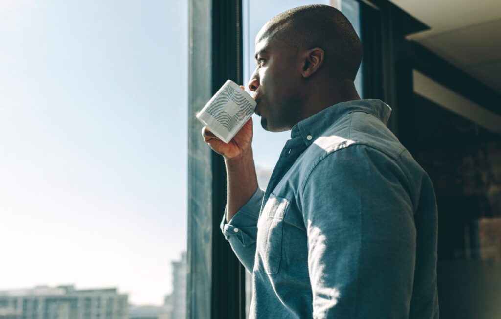 Pensive young man having a cup of coffee while looking out the window